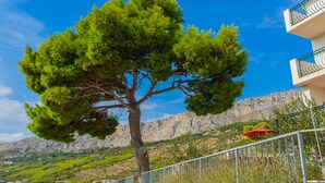 Un arbre devant un immeuble avec un balcon et un parasol rouge.