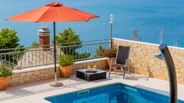 Un espace aménagé au bord de la piscine, avec un parasol rouge, une chaise et des plantes en pot.