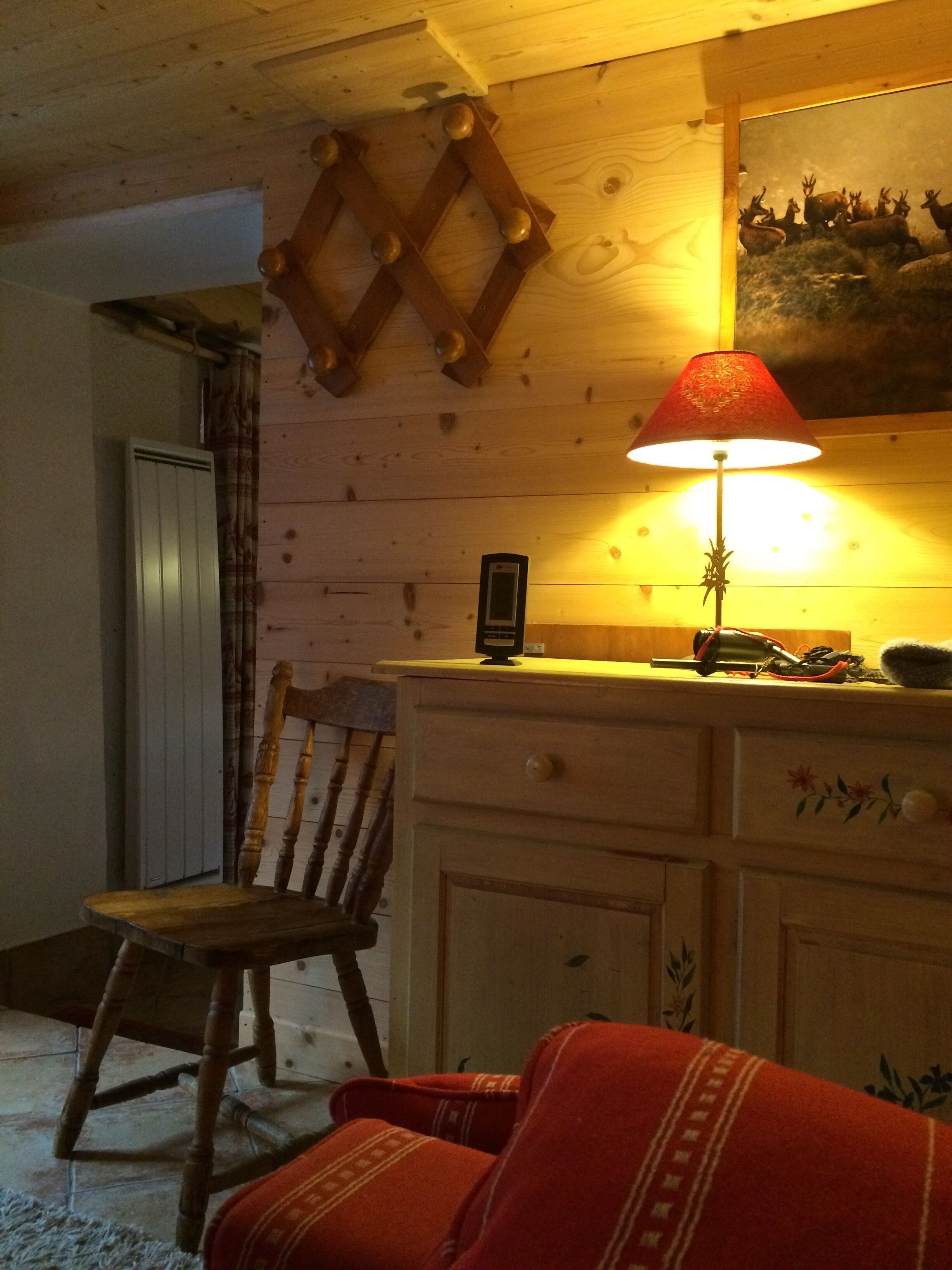 Una habitación acogedora con paredes de madera, una silla de madera, un sofá rojo, una lámpara y un cuadro de ciervos.