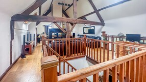 Ein geräumiger Loft-Raum mit freiliegenden Holzbalken, einer Holztreppe und einem großen Fenster, das für natürliches Licht sorgt.