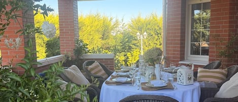 An outdoor dining area with wicker furniture and a table set for a meal, surrounded by brick walls and greenery.
