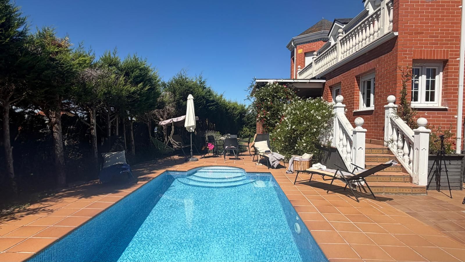 Ein Schwimmbecken mit Fliesen umgeben, mit Liegestühlen und einem Ziegelhaus mit Balkon.