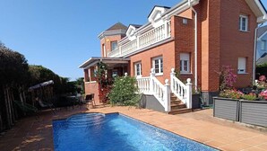A large rectangular swimming pool with a tiled deck, surrounded by a brick house with a balcony and a staircase leading to the entrance. - Monte & Mar House (Camargo)