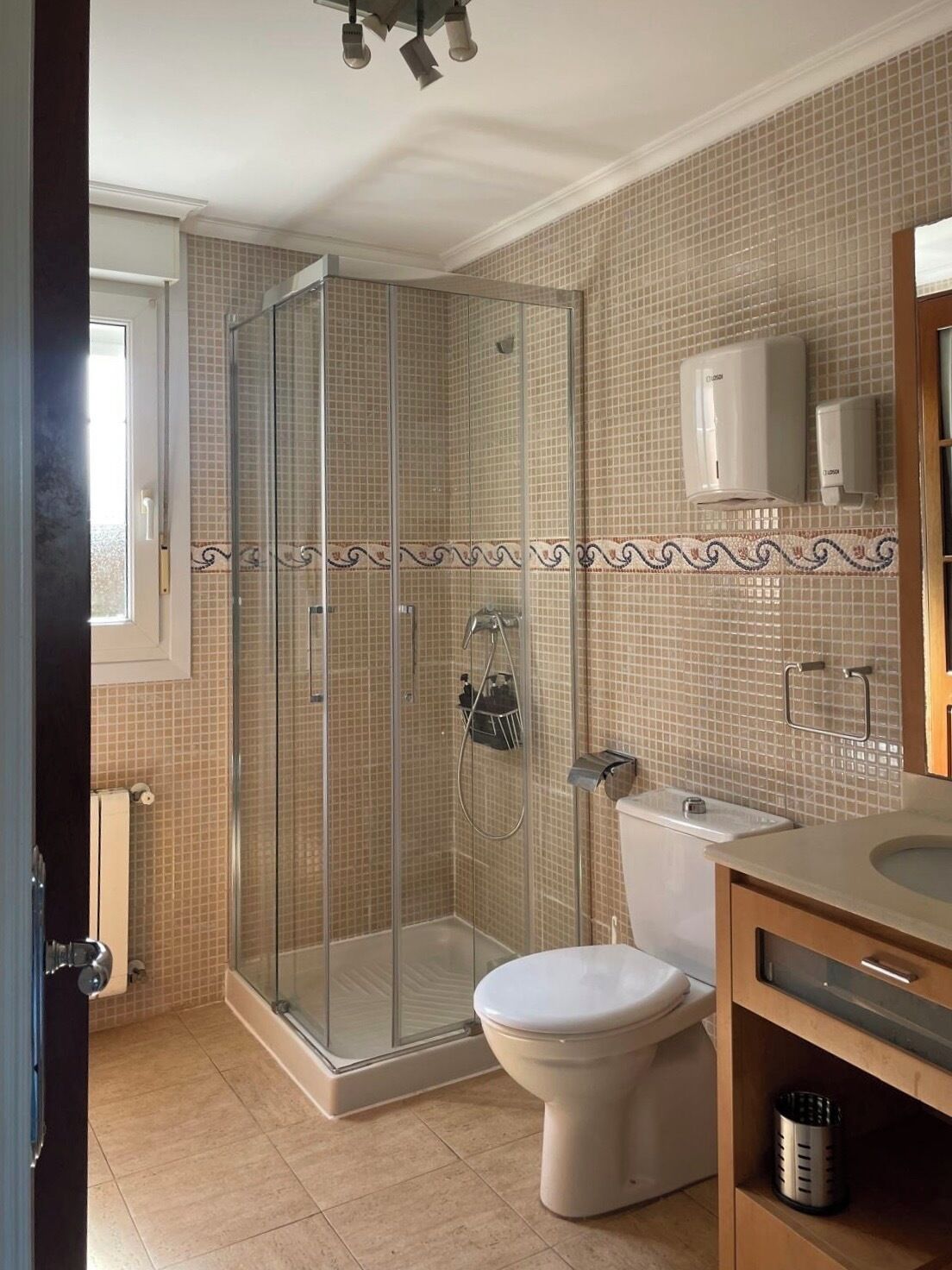 A bathroom with a glass-enclosed shower, a toilet, and a sink.