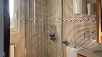 A bathroom with a glass-enclosed shower, a toilet, and a sink.