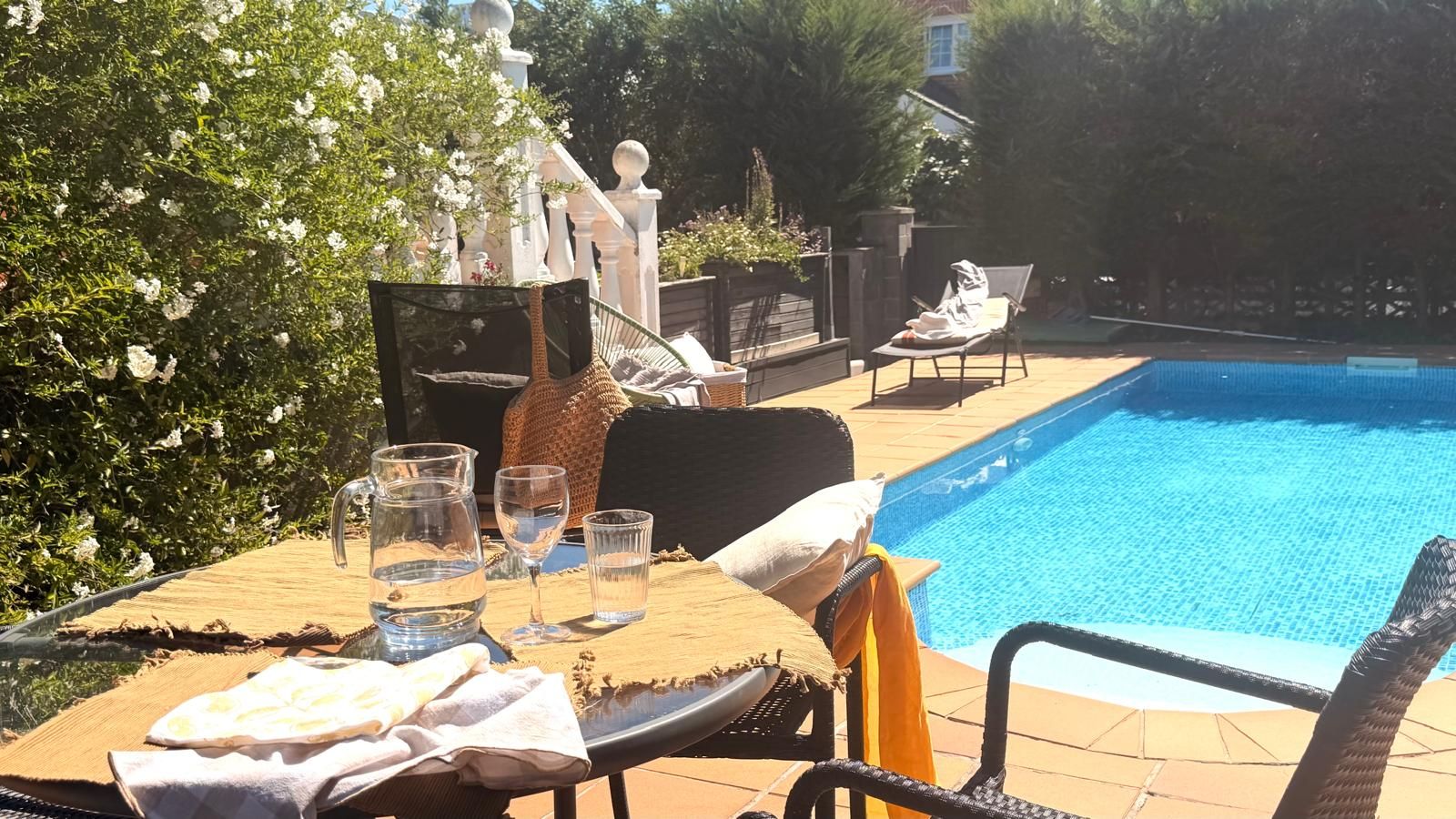A poolside area with a table set for two, a chair, and a lounge chair.