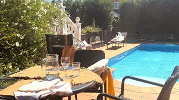A poolside area with a table set for two, a chair, and a lounge chair.