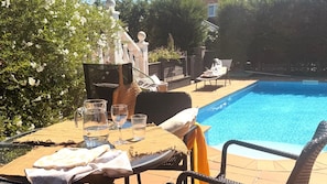 A poolside area with a table set for two, a chair, and a lounge chair.