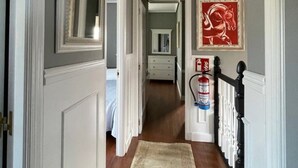 A hallway with a wooden floor, white walls, and a black railing. There is a fire extinguisher mounted on the wall. - Monte & Mar House (Camargo)