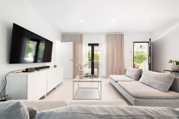 A modern living room with a flat-screen TV, a sofa, a coffee table, and a view of the outdoors. - Villa Claudine,  800 meters from the beach with pool, for 6 People (Alcúdia)