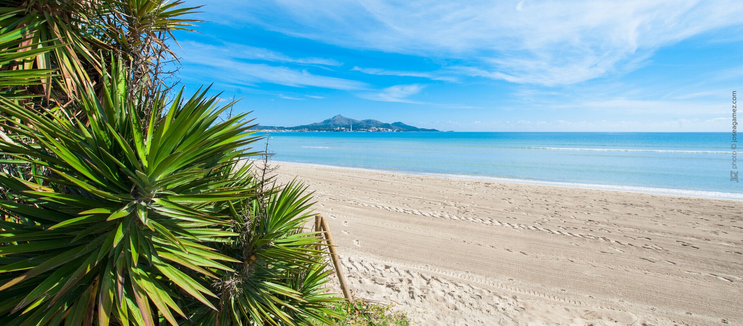 Una playa con cielos despejados, una orilla arenosa y una montaña a lo lejos.