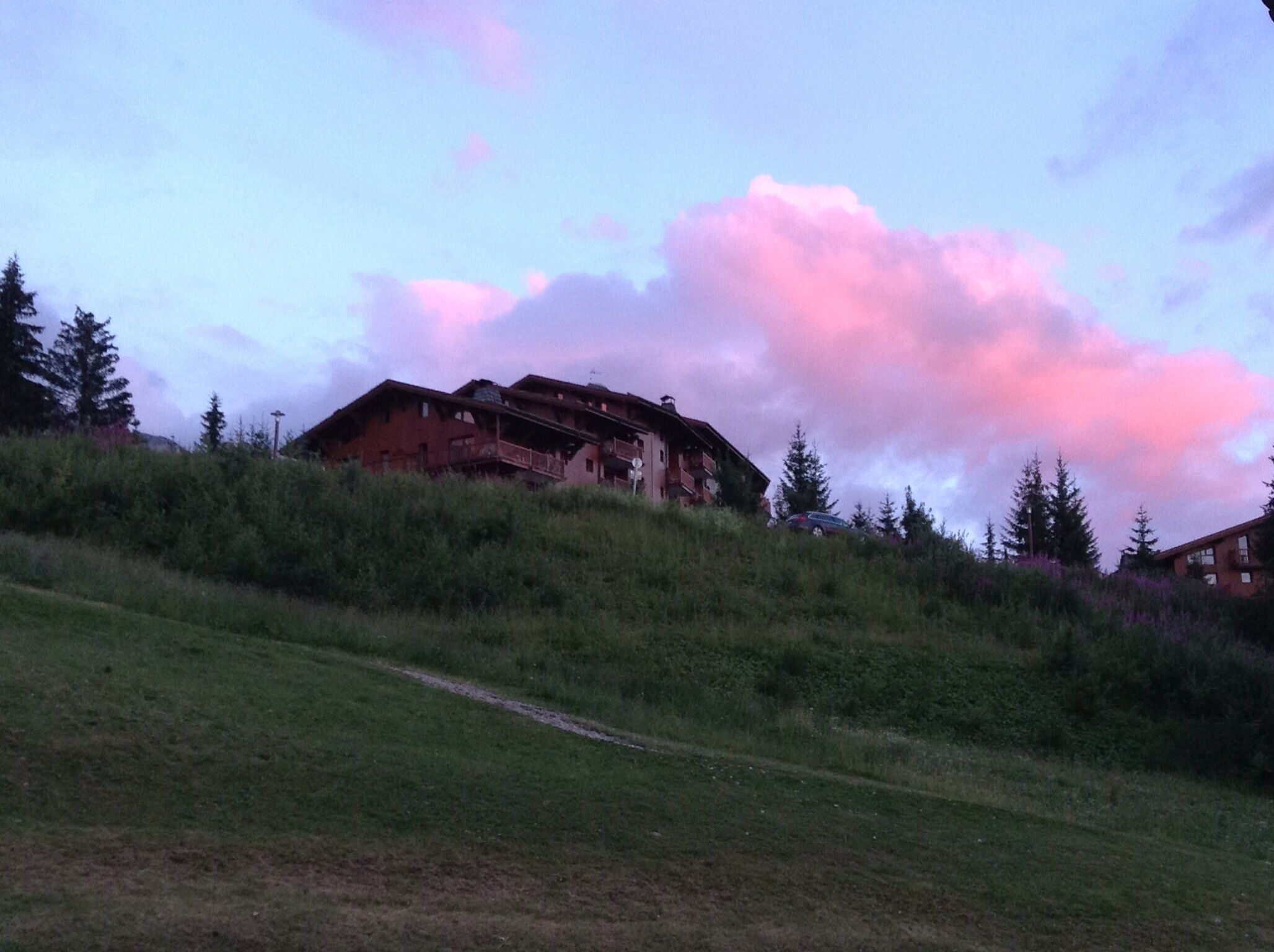 Un bâtiment rustique, doté d’un toit en pente, situé sur une colline herbeuse, entourée d’une végétation luxuriante.
