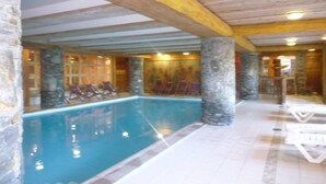 Ein Innenpool mit Steinsäulen, Liegestühlen und einer Holzbalkendecke.