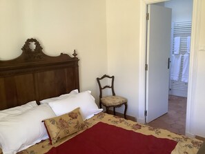 A bedroom with a wooden headboard, a single bed with white and beige bedding, a floral-patterned pillow, a red throw blanket, and a wooden chair. - Lovely house, garden with pool in tranquil village near coast and countryside (Raissac-D'aude)