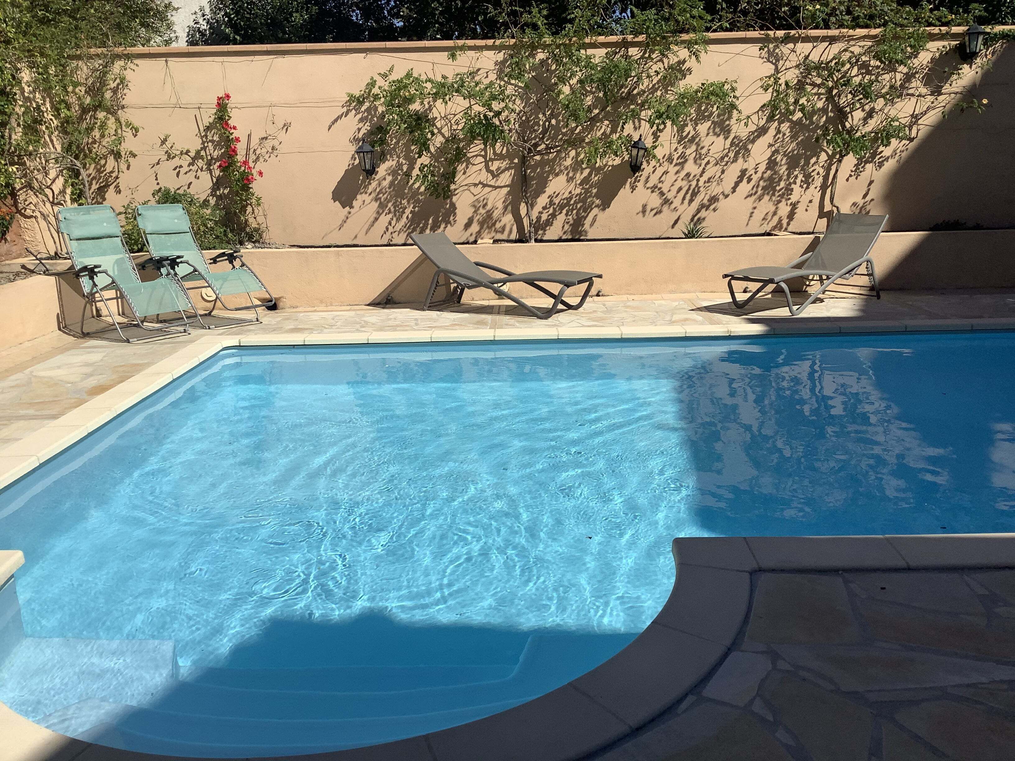 Een rechthoekig zwembad met helderblauw water, omgeven door een beige muur en een betegeld terras.