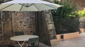 An outdoor patio with a stone table and chairs, a white umbrella, and a swimming pool. - Lovely house, garden with pool in tranquil village near coast and countryside (Raissac-D'aude)