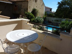 A balcony with a round table and two chairs, overlooking a swimming pool and lush greenery. - Lovely house, garden with pool in tranquil village near coast and countryside (Raissac-D'aude)
