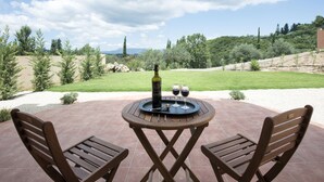 Un patio con dos sillas de madera, una mesa con una botella y vasos, y vistas a un paisaje verde.