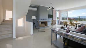 Un amplio salón con escaleras, chimenea y comedor con sillas y mesa.