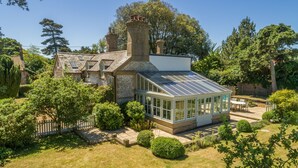 A traditional house with a conservatory, surrounded by a well-maintained garden and a wooden fence.