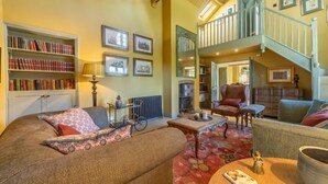 A cozy living room with a high ceiling, a staircase, a bookshelf, and a fireplace.