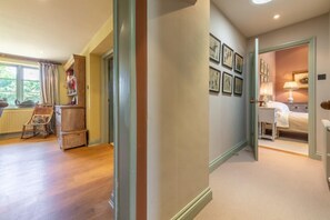 A hallway leading to a bedroom with a bed, a nightstand, and a lamp. There are framed pictures on the wall and a window with curtains. - The Old School House (W), Warham, Norfolk (Warham)