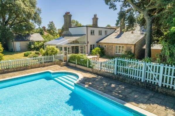 A swimming pool with a white fence, a conservatory, and a house with chimneys. - The Old School House (W), Warham, Norfolk (Warham)