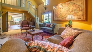 A spacious living room with a high ceiling, a staircase, and a large map on the wall.