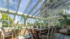 A conservatory with a glass ceiling, a dining table with chairs, and a chandelier.