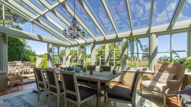 A conservatory with a wooden table and chairs, large windows, and a chandelier.