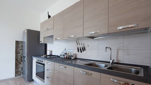 A modern kitchen with light wood cabinets, stainless steel appliances, and a black countertop. - Two steps outside 5 terre, Casa Sterinella !! (Follo Alto)