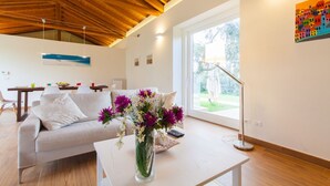 Een moderne woonkamer met een houten plafond, een groot raam, een bank, een salontafel en een bloevas.