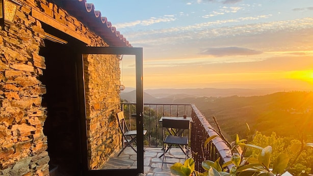 Un edificio de piedra con un balcón que da a un paisaje montañoso al atardecer.