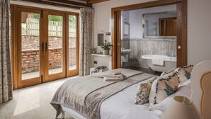 A bedroom with a large bed, a bathroom with a bathtub, and a view of a stone wall and wooden fence outside. - Luxury Farmhouse with Stunning Somerset Views (Taunton)
