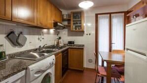 A compact kitchen with wooden cabinets, a built-in oven, a washing machine, and a dining area with a table and chairs. - Venice historic center 5 minutes from the Rialto Bridge (Venezia)