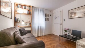 A living room with a sofa, a wooden bookshelf, a door, and a small table with a vase and a remote control. - Venice historic center 5 minutes from the Rialto Bridge (Venezia)