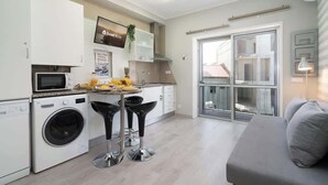 A modern kitchen with a washing machine, microwave, and bar stools. - Sweet Cozy Flat w/ Balcony by HostWise (Porto)