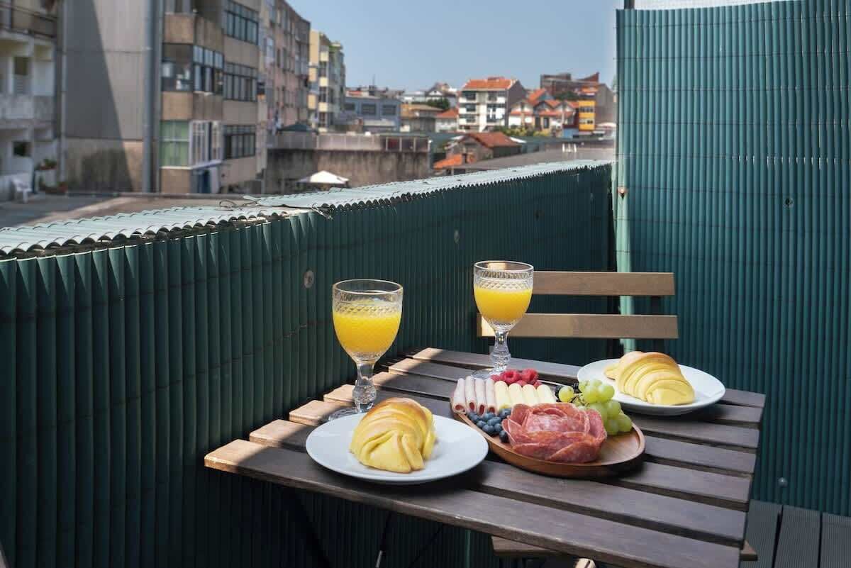 Une table de petit-déjeuner avec des croissants, des fruits et des verres de jus, placée sur un balcon donnant sur une vue panoramique de la ville.