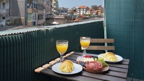 A breakfast table with croissants, fruit, and juice glasses on a balcony overlooking a cityscape. - Sweet Cozy Flat w/ Balcony by HostWise (Porto)