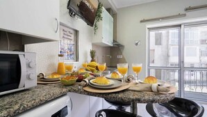A kitchen with a microwave, a toaster, and a coffee maker. There is a breakfast spread on the counter with fruits, bread, and orange juice. - Sweet Cozy Flat w/ Balcony by HostWise (Porto)