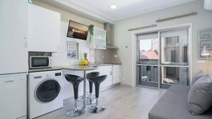 A compact kitchen with a microwave, washing machine, and a small dining area with two stools. - Sweet Cozy Flat w/ Balcony by HostWise (Porto)
