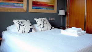 A neatly made bed with white bedding and black patterned pillows, a lamp, and two framed paintings on the wall.