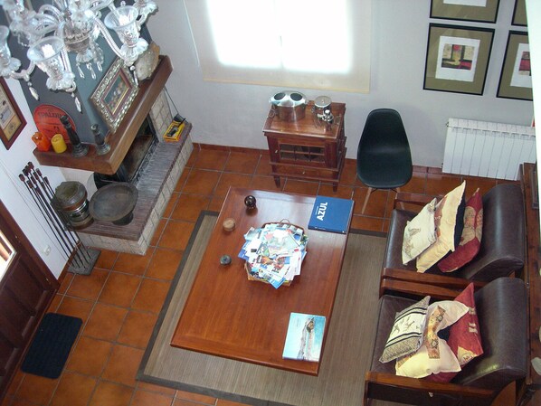 A living room with a wooden coffee table, a sofa, and a fireplace. There are framed pictures on the wall and a window providing natural light.