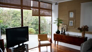 A living room with a large flat-screen TV, a wicker chair, a wooden console table, and framed artwork on the wall.