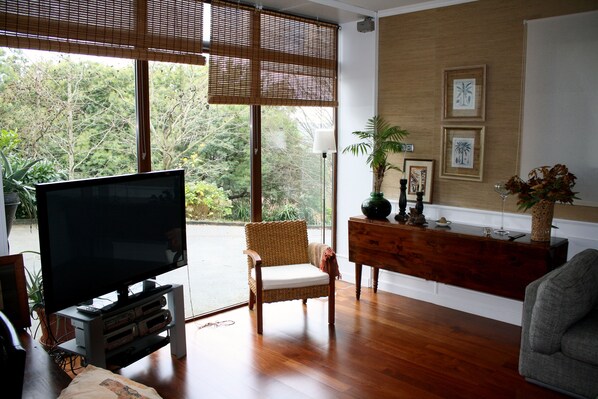 Una sala de estar con un televisor de pantalla plana grande, un sillón de mimbre, una consola de madera y obras de arte enmarcadas en la pared.