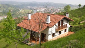 A two-story house with a tiled roof, a balcony, and a view of a valley.