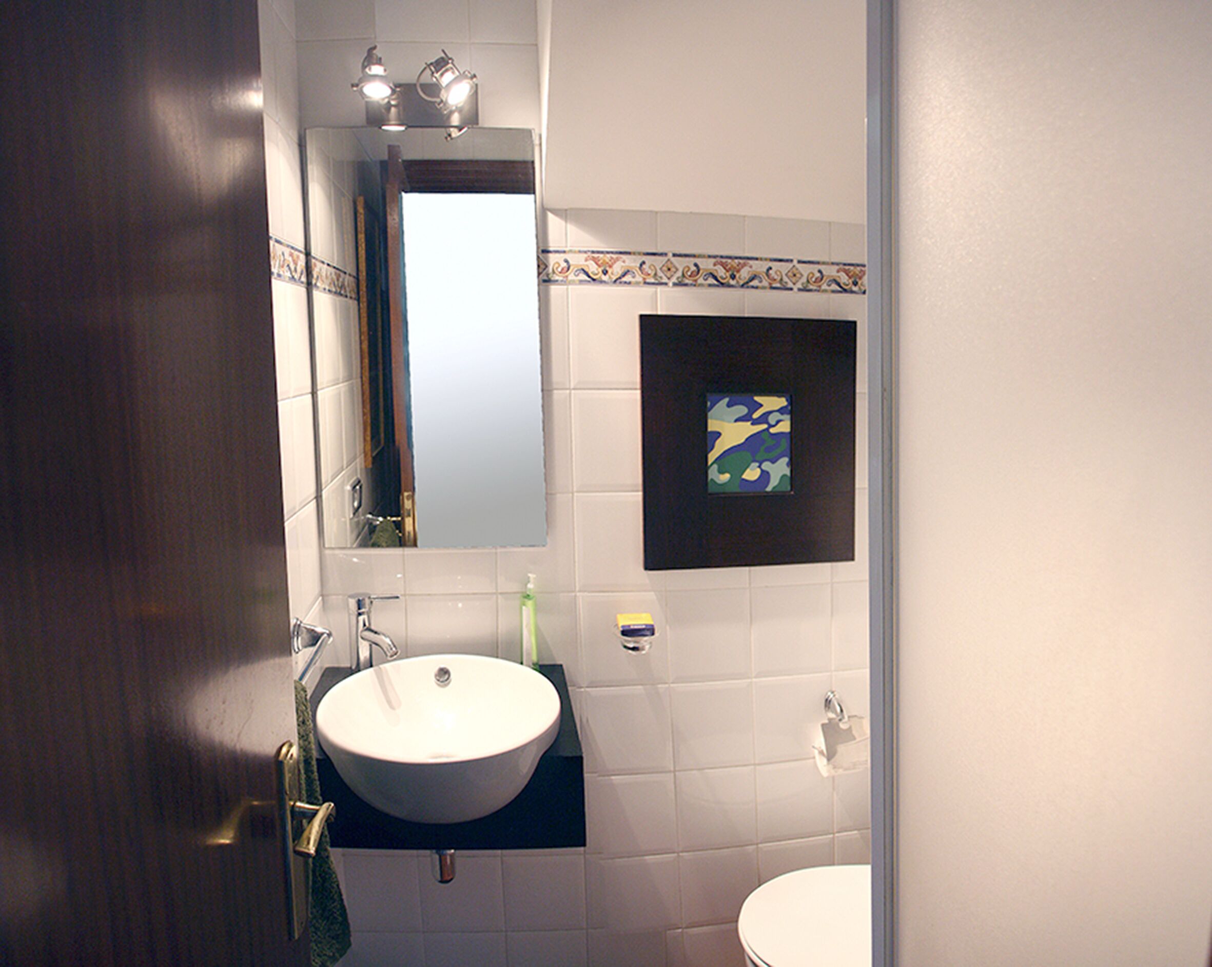 A bathroom with a white sink, a mirror, and a small framed artwork on the wall.