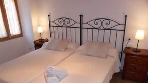 Un lit double avec une tête de lit en métal, deux tables de chevet avec des lampes et une serviette roulée posée sur le lit.