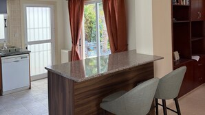Una cocina con una isla central, taburetes de bar, una estantería empotrada y un ventanal con cortinas.