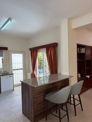 Una cocina con una isla central, taburetes de bar, una estantería empotrada y un ventanal con cortinas.